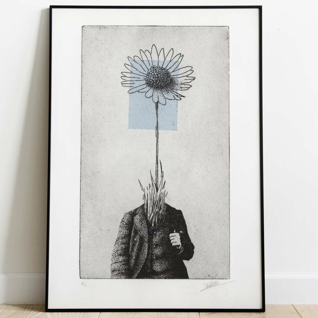 Gravure surréaliste "Bellis perennis" dans un grand cadre noir fin, posée au sol sur un parquet en bois clair contre un mur blanc. L'œuvre verticale montre un personnage en costume dont la tête est remplacée par une grande marguerite sur fond bleu.