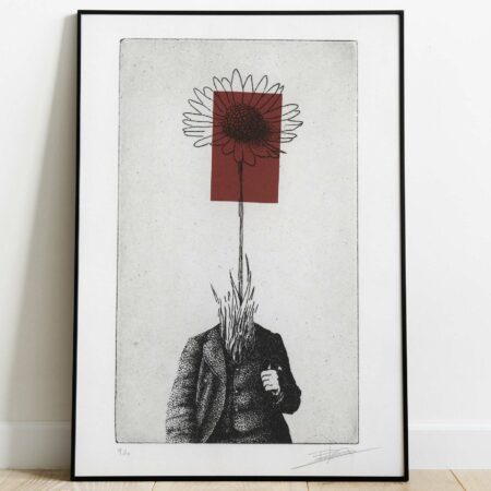 Gravure surréaliste "Bellis perennis" dans un grand cadre noir fin, posée au sol sur un parquet en bois clair contre un mur blanc. L'œuvre verticale montre un personnage en costume dont la tête est remplacée par une grande marguerite sur fond rouge.