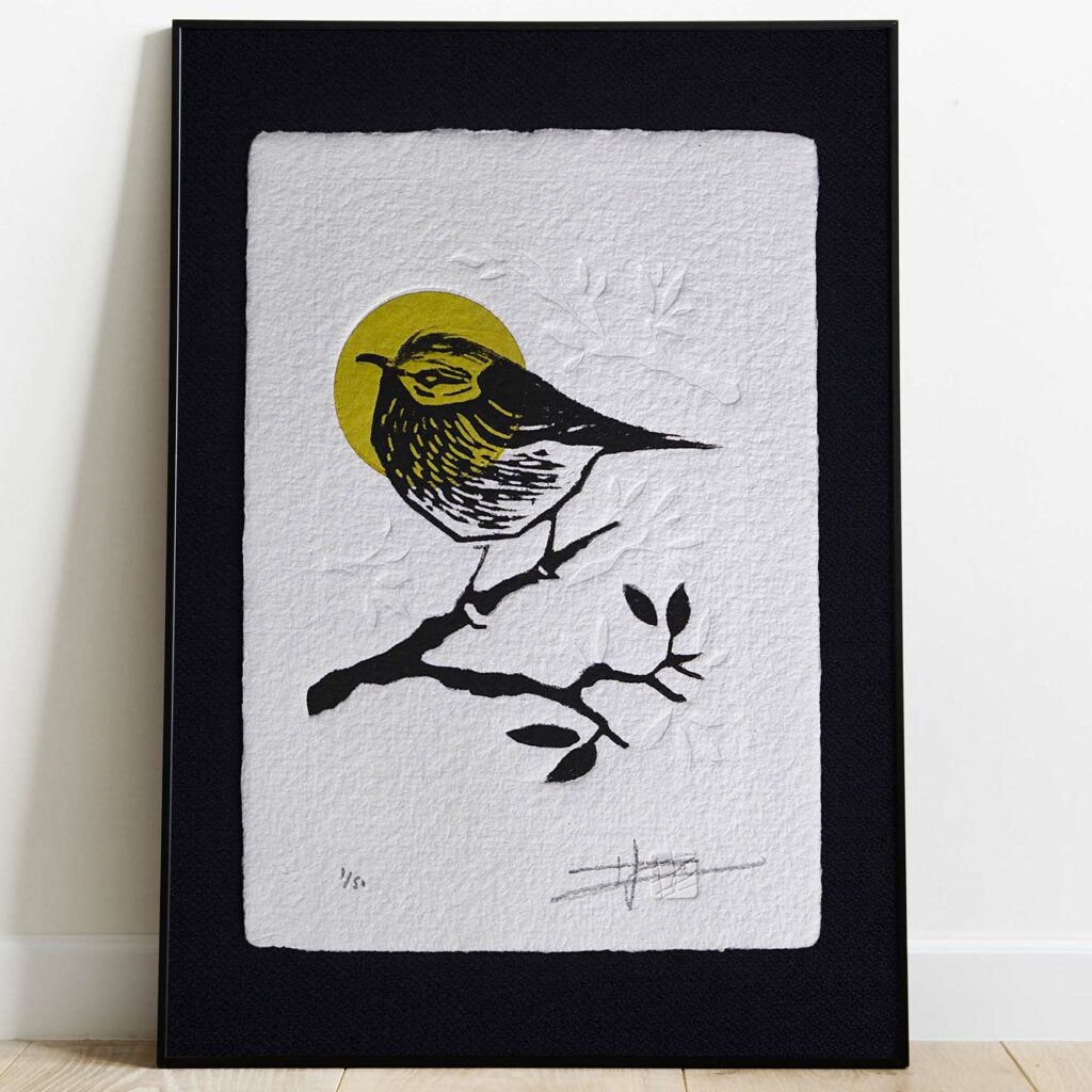 Gravure "Golden Crown Kinglet" sur papier d'art blanc épais et texturé à bords frangés, présentée dans un cadre noir texturé, posée sur un parquet en bois clair contre un mur blanc.