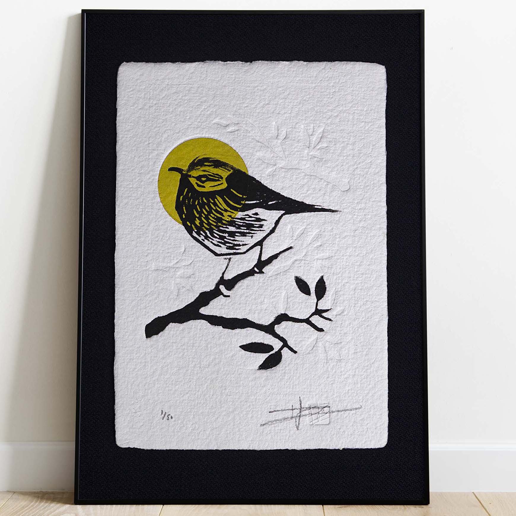 Gravure "Golden Crown Kinglet" sur papier d'art blanc épais et texturé à bords frangés, présentée dans un cadre noir texturé, posée sur un parquet en bois clair contre un mur blanc.