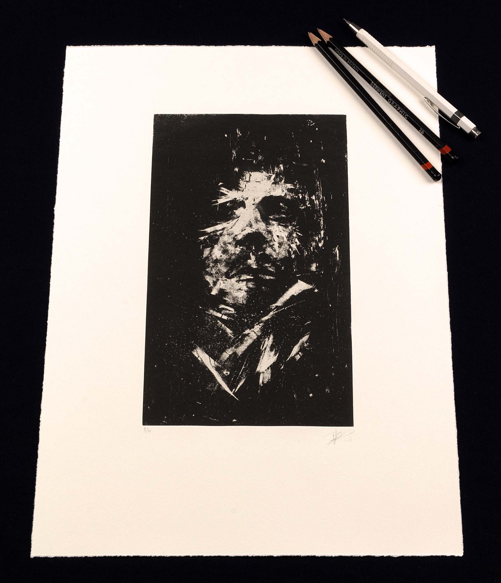 Gravure expressionniste en noir et blanc "Portrait" dans un grand cadre noir fin avec un passe-partout blanc, posée au sol sur un parquet clair contre un mur blanc.