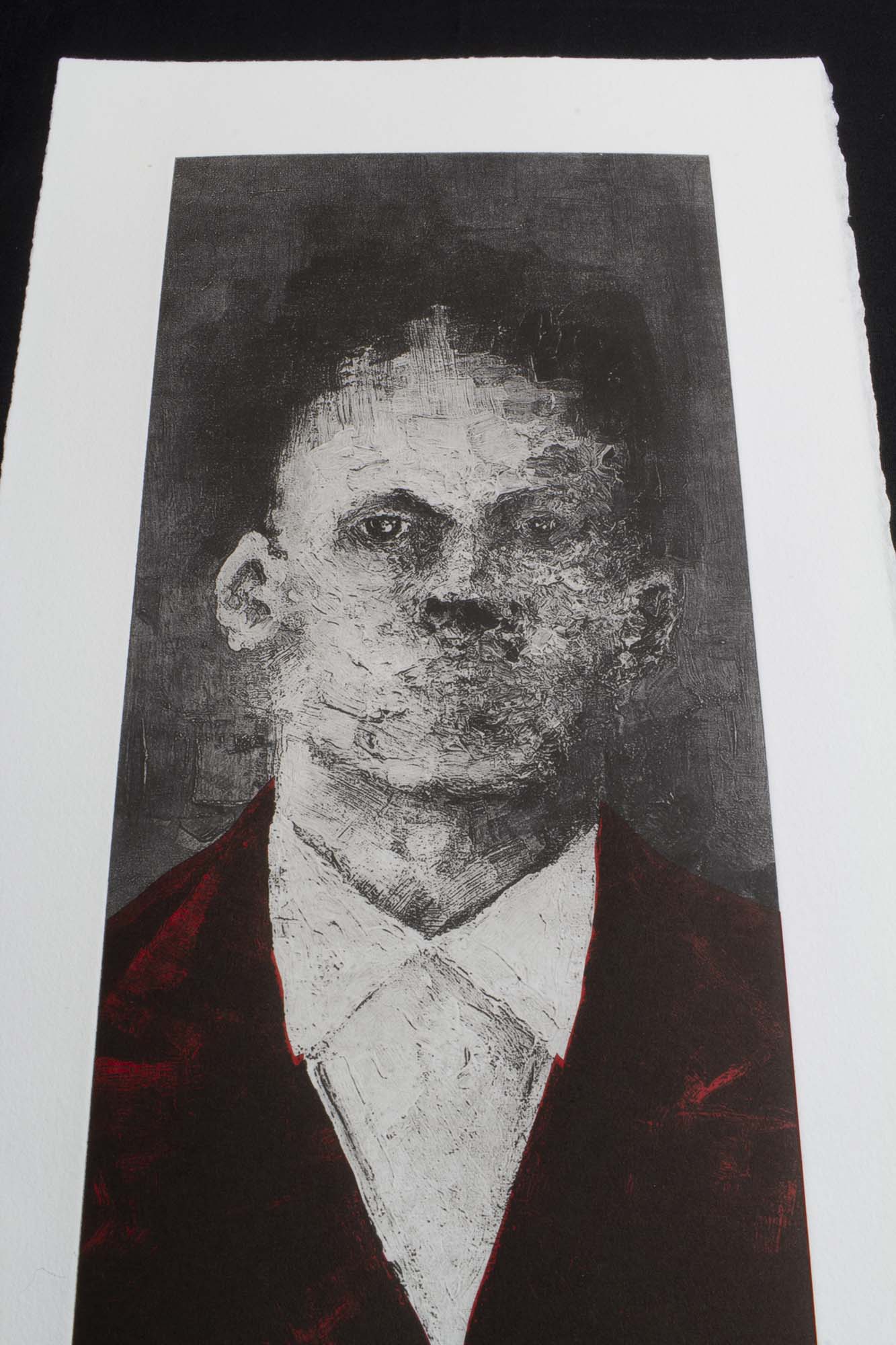 Gravure expressionniste "Portrait XXI" dans un grand cadre noir fin, posée au sol sur un parquet en bois clair contre un mur blanc. L'œuvre verticale représente un homme en costume sombre rehaussé de rouge.
